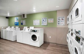 A laundry facility with multiple washing machines and dryers, instructional posters on the wall, and a clean, organized layout.