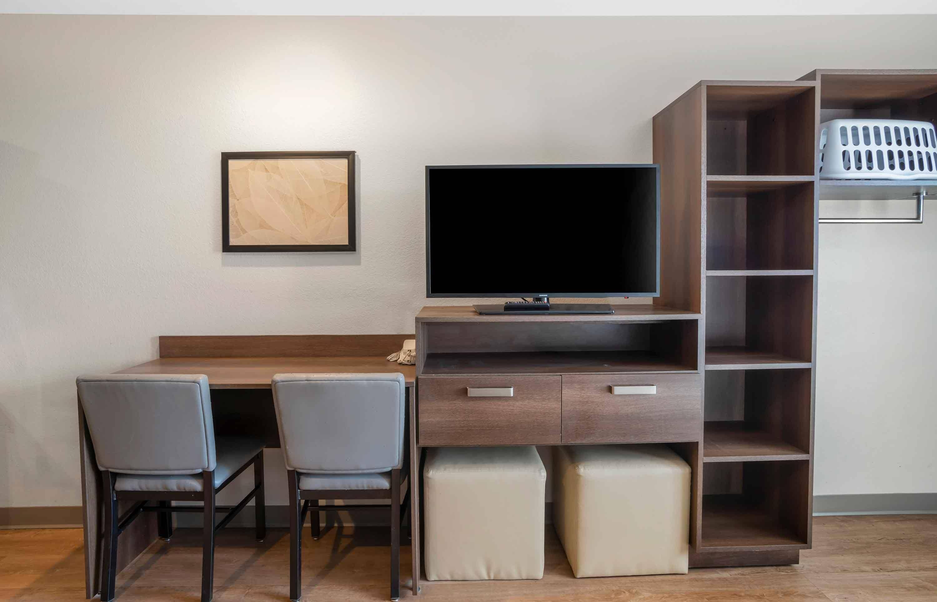 Een moderne woonkamer met een houten bureau, een flatscreen televisie, twee stoelen, een bank en een inbouwplank.