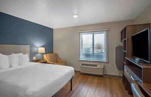 A hotel room with a bed, a chair, a TV, and a window with blinds.