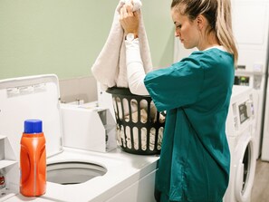 A person in teal scrubs hanging a white towel on a washing machine.