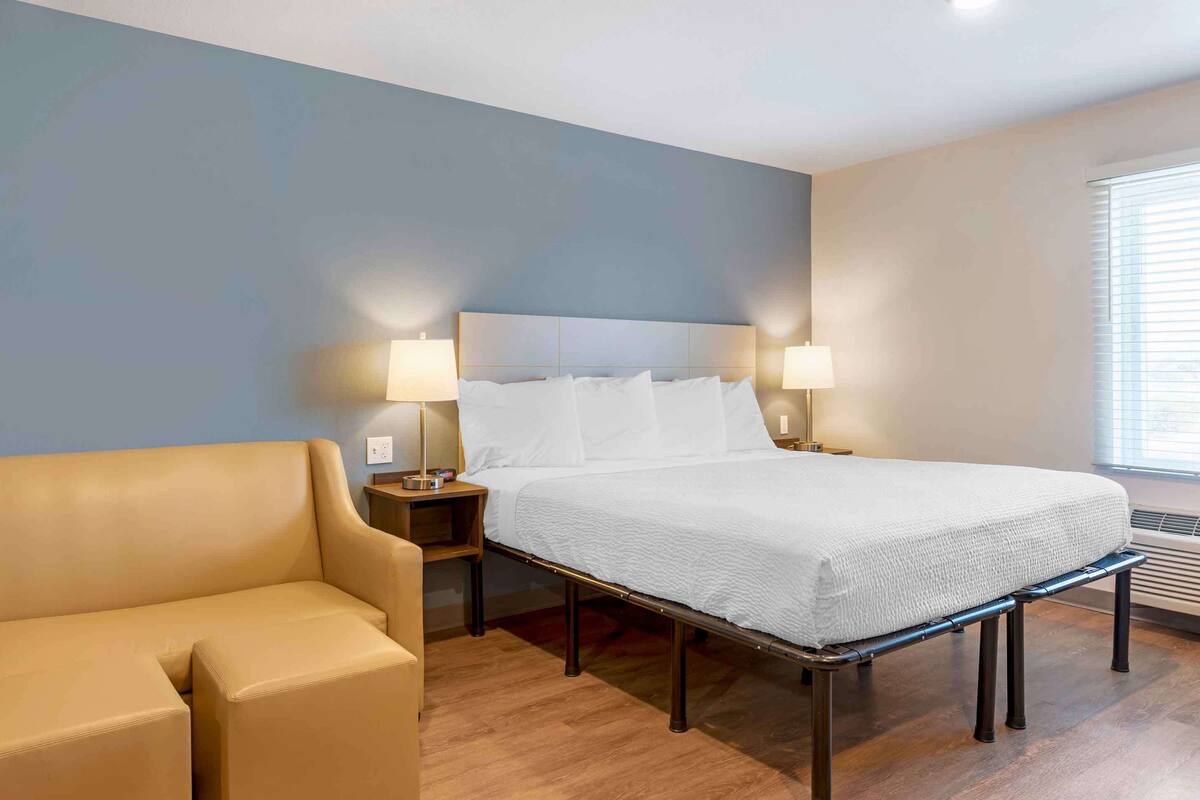 A hotel room with a bed, two bedside tables with lamps, a sofa, and a window with blinds.