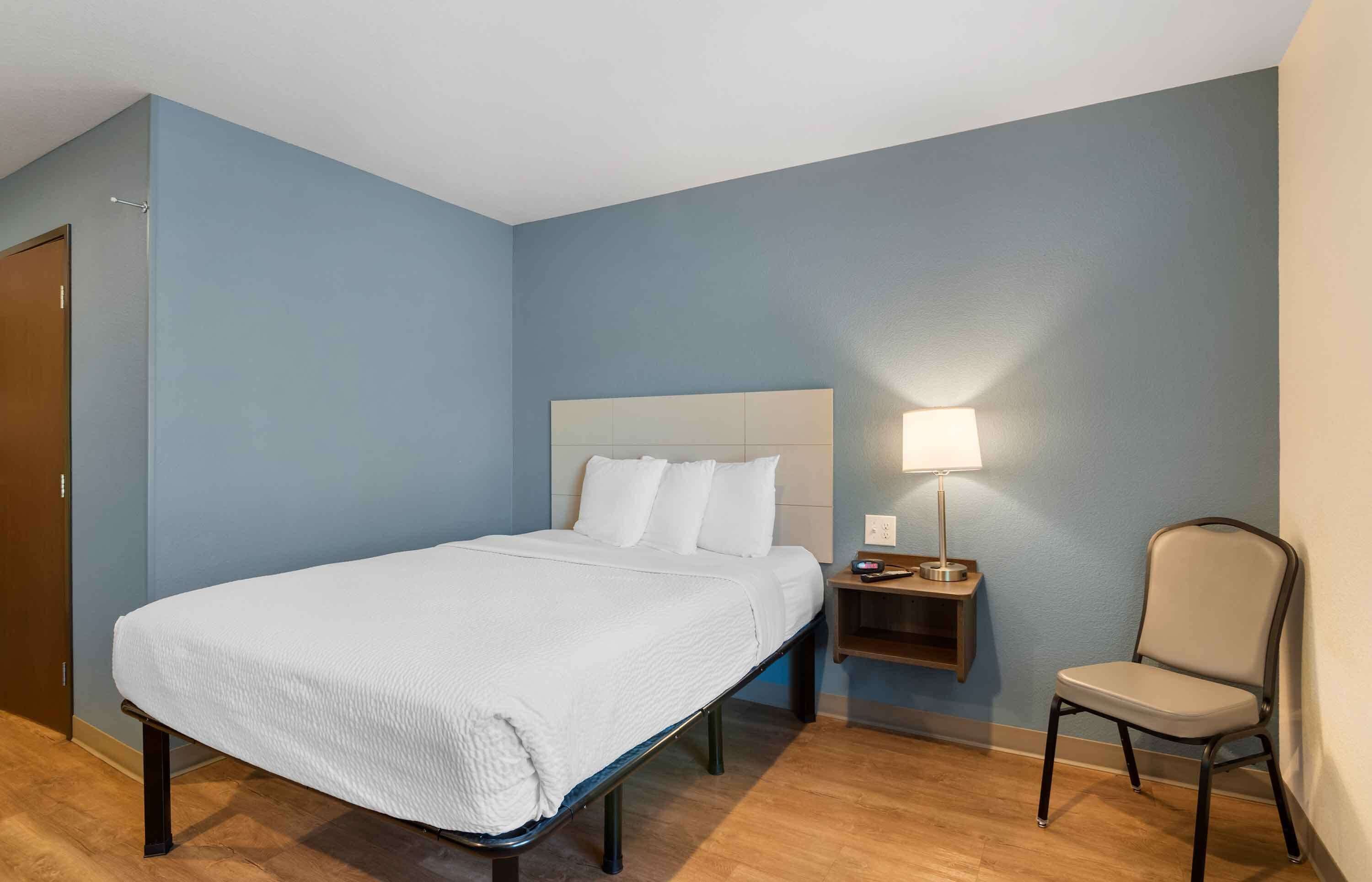 Habitación de hotel con cama, mesita de noche, lámpara y silla.