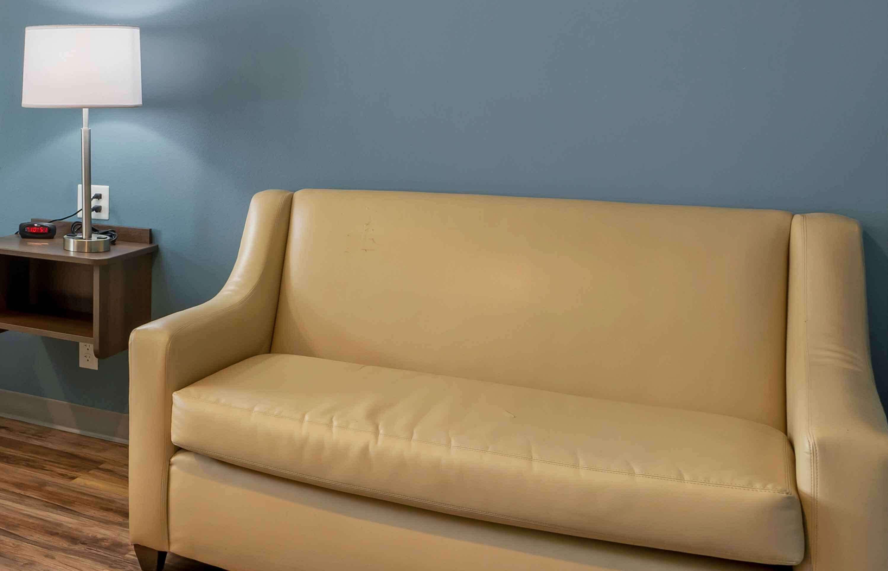 A beige sofa against a blue wall, a small table with a lamp, and a power outlet.