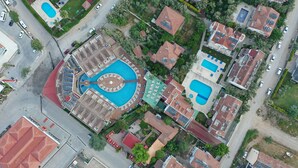 Vista aérea de una zona residencial que muestra una piscina circular grande rodeada por una terraza cubierta, varias casas independientes y un campo deportivo.