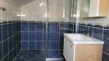 Een badkamer met een douchecabine van glas, een witte wastafel en een houten wastafelmeubel.