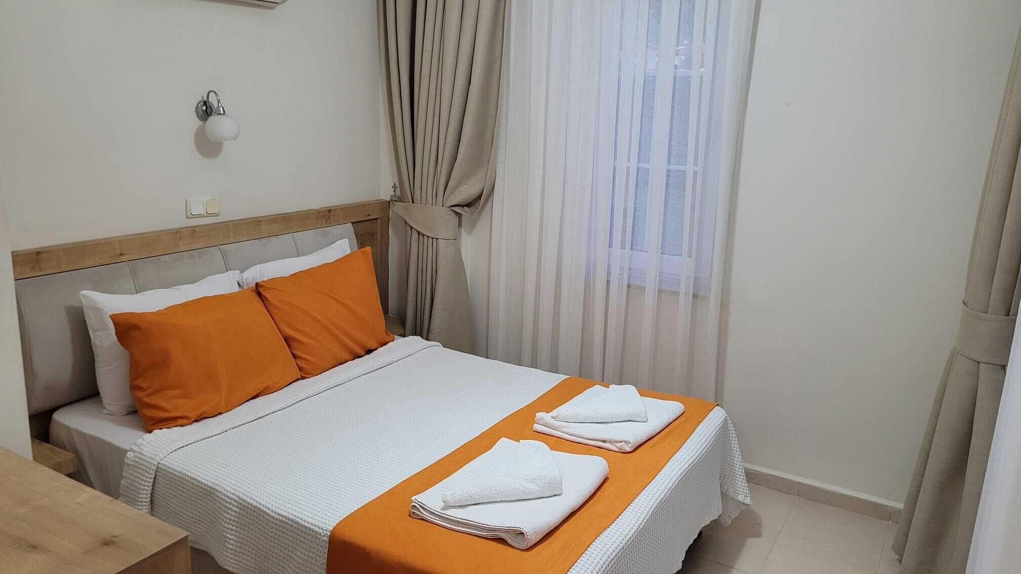A hotel room with a bed, two pillows, a nightstand, a lamp, and a window with curtains.