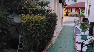 Uma passagem estreita com piso verde que conduz a um edifício com fachada branca e telhado vermelho.