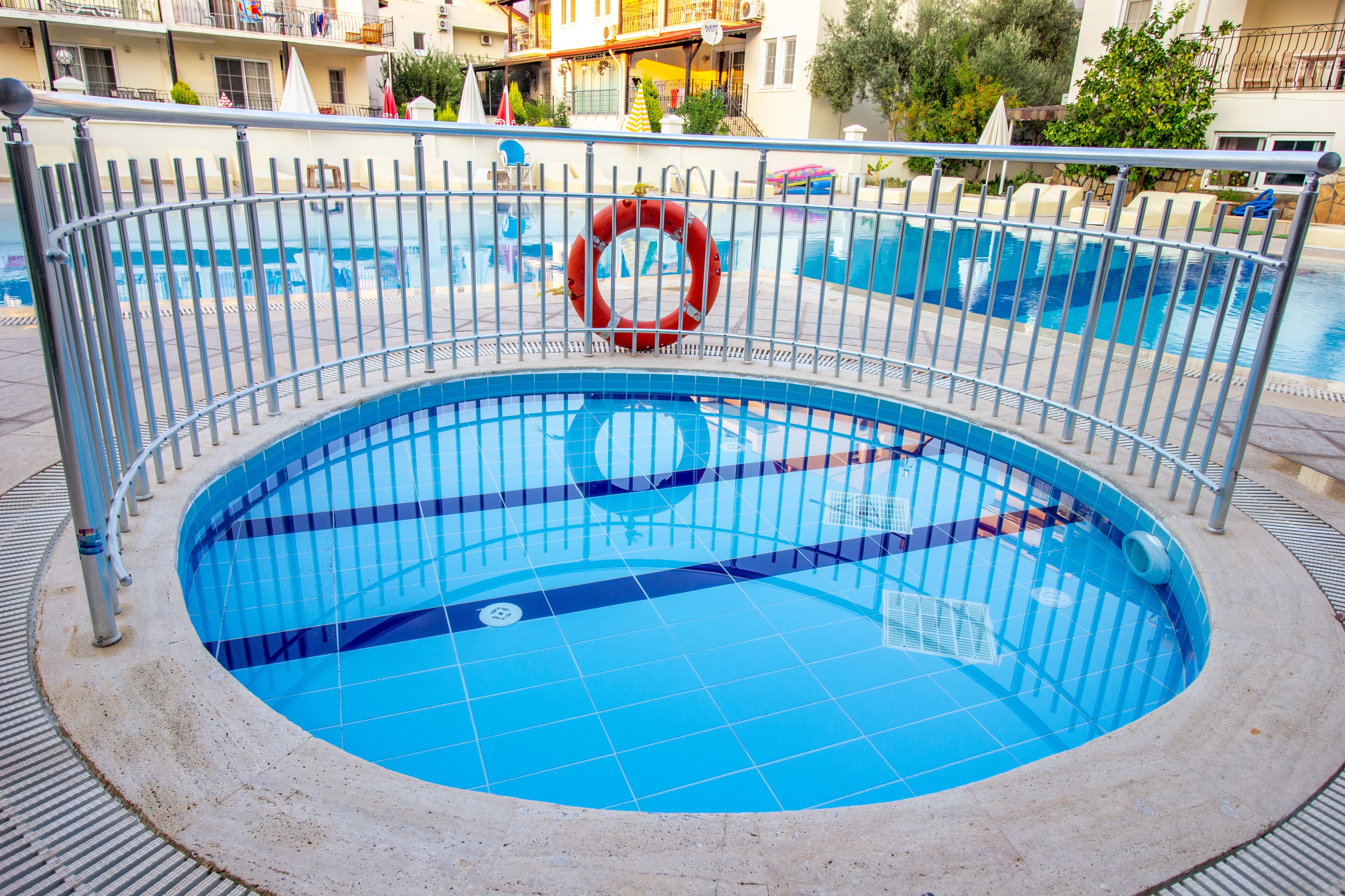 A swimming pool with a metal railing, a lifebuoy, and a tiled deck.