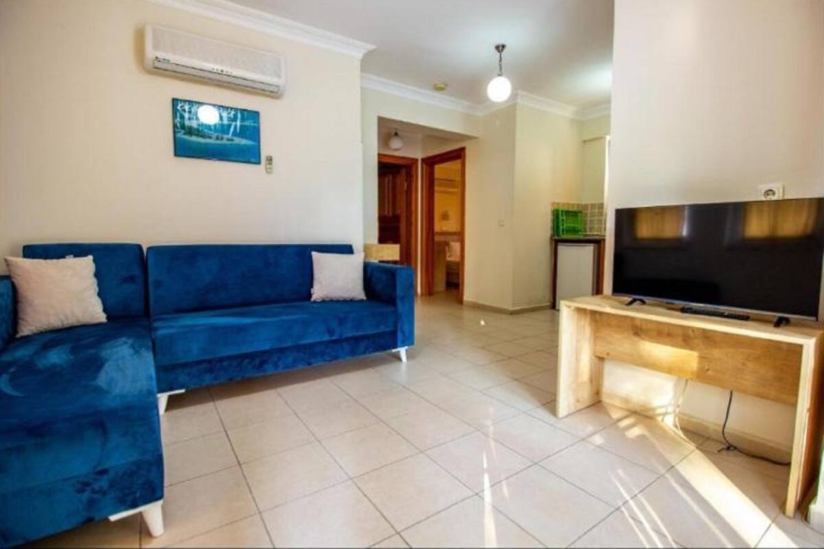 A living room with a blue sofa, a wooden TV stand, and a tiled floor.