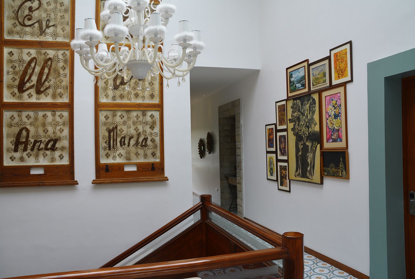 Una escalera con barandilla de madera, un candelabro y cuadros en las paredes.