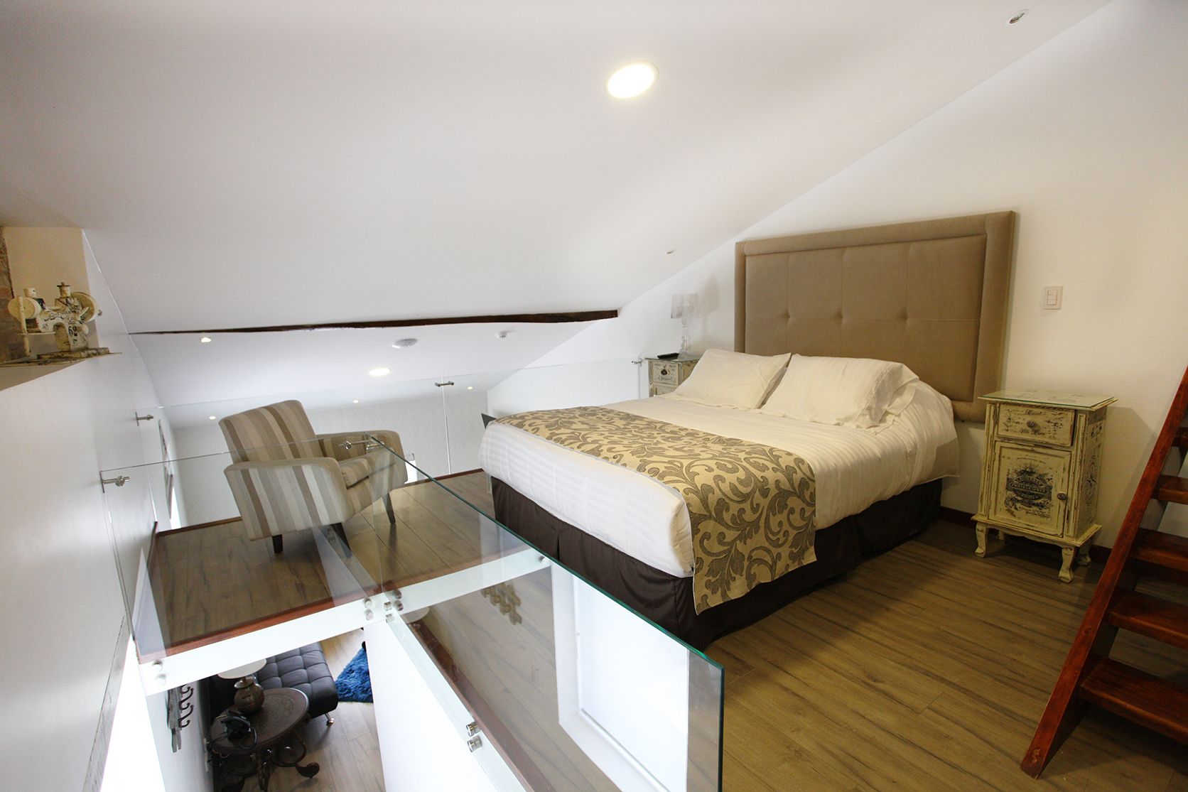 Un dormitorio con una cama, un escritorio de cristal, una silla, una mesita de noche y una escalera.