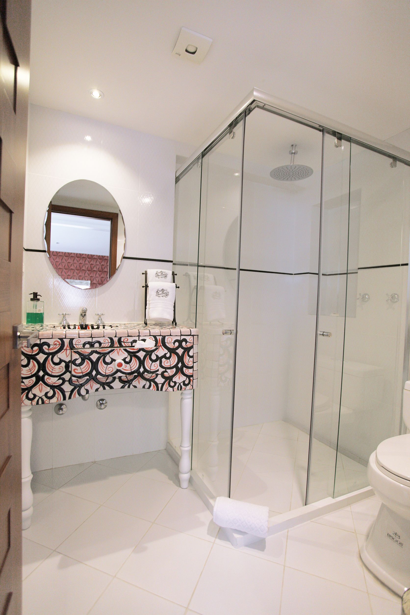 Un baño con ducha de vidrio, inodoro blanco y lavamanos con diseño.