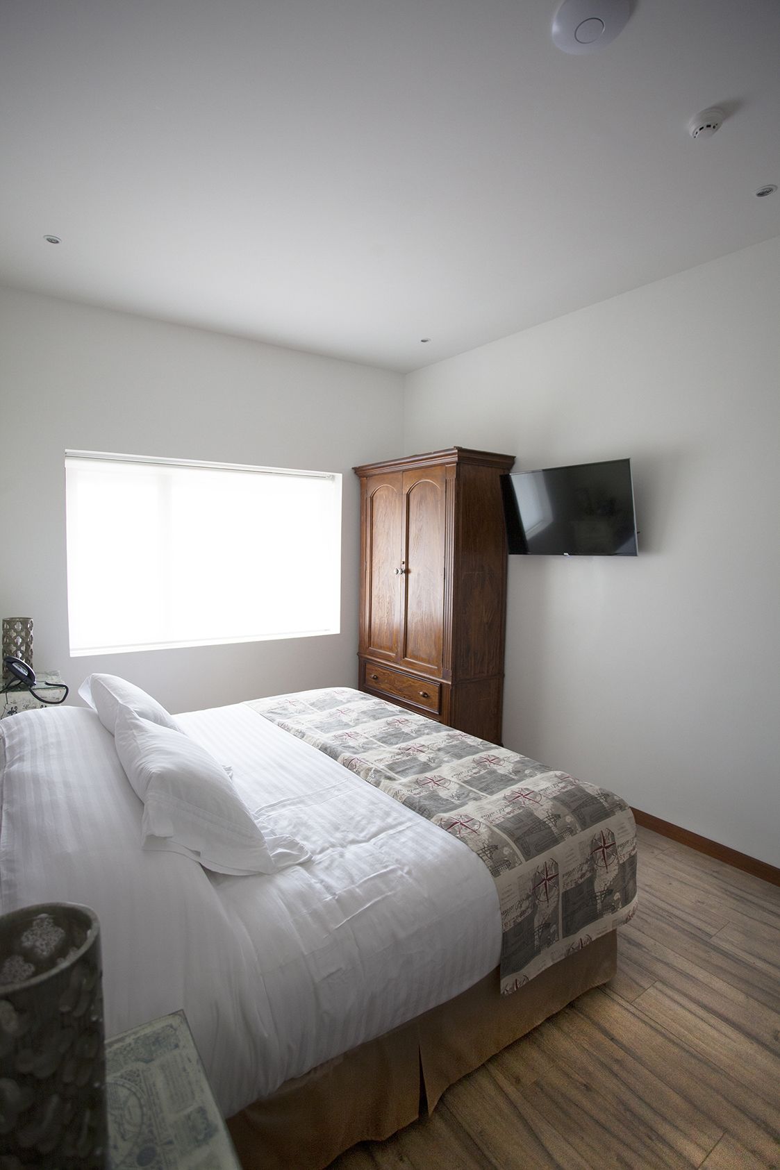 Un dormitorio con cama, armario de madera, televisor de pantalla plana montado en la pared y ventana con persianas.