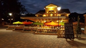 A building with a central patio area featuring outdoor seating under colorful umbrellas, a brick-paved ground, and a signboard with a menu. - Villa Ana Maria Cuenca (Cuenca)