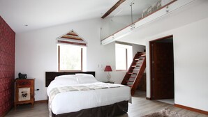 Um quarto com uma cama grande, um penteou de madeira, uma escrivaninha, um abajur, uma janela e uma escada.