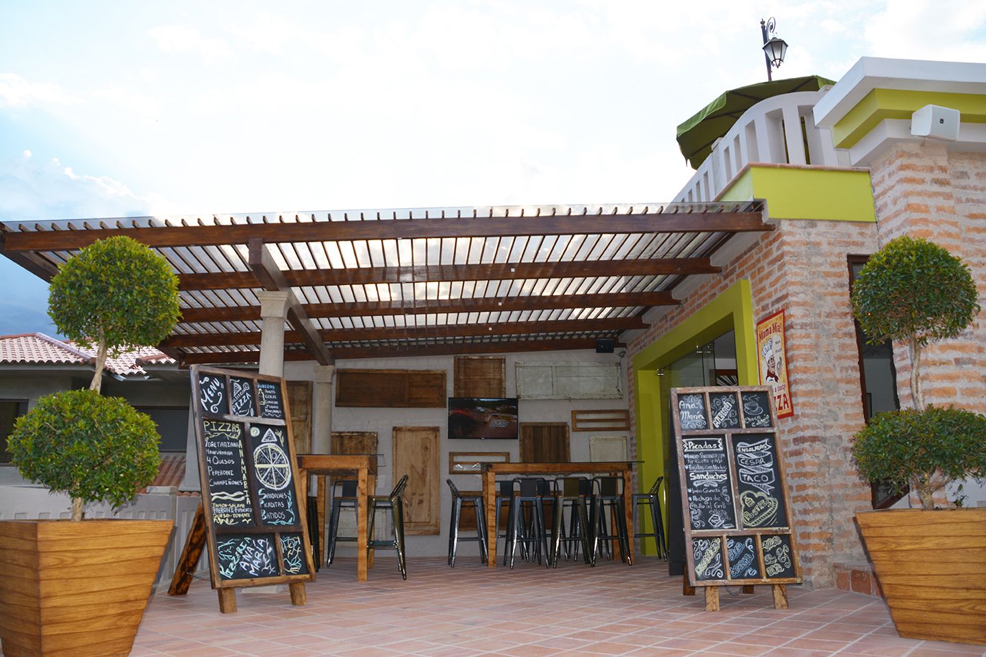 Ein Außenbereich mit Holztischen und -stühlen, umgeben von Backsteinmauern und einer Pergola.