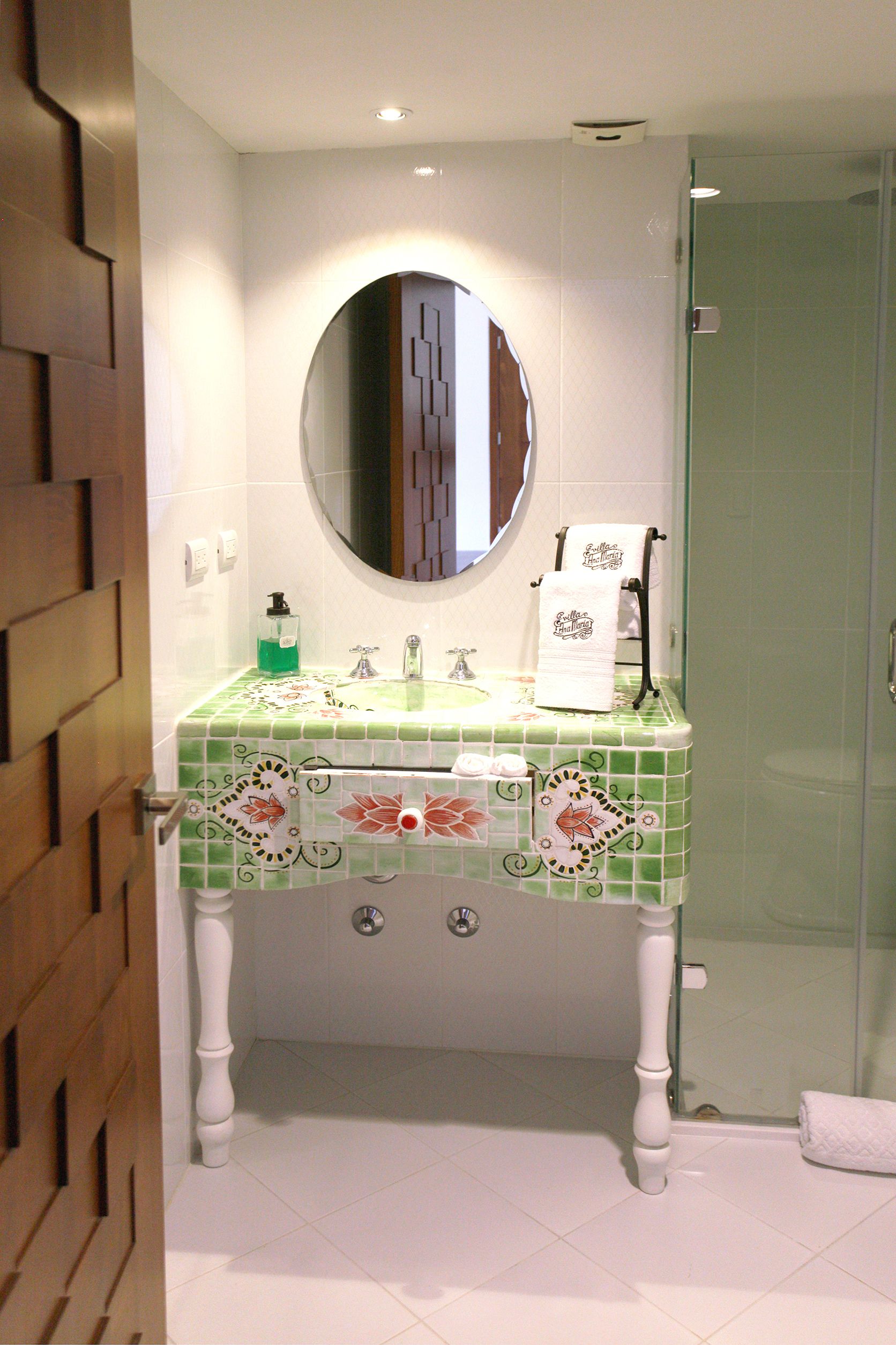 A bathroom with a green tiled sink, a mirror, a towel rack, and a glass shower door.