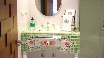 A bathroom with a green tiled sink, a mirror, a towel rack, and a glass shower door.