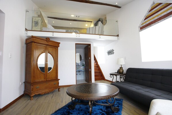 Amplia sala de estar con techo alto, un mueble de madera con espejo, una mesa redonda de centro, un sofá negro y una escalera que conduce a un nivel superior.
