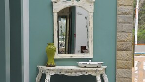 Um quarto com parede verde, um console branco ornamentado, um espelho, um vaso verde e pufes estampados.