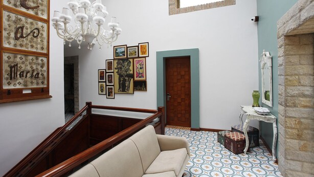 A spacious room with a wooden staircase, a chandelier, and a variety of framed artworks on the walls. - Villa Ana Maria Cuenca (Cuenca)