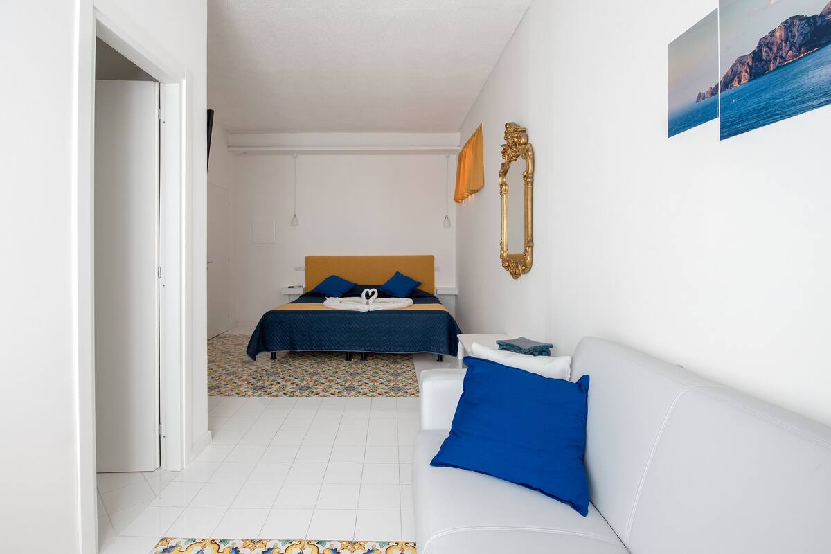 A bedroom with a bed, a white sofa, a patterned rug, and a framed picture on the wall.