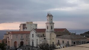 A historic building with a prominent bell tower and a clock, featuring a traditional architectural style with a red-tiled roof and a view of the sea in the background. - Sunset Rooms (Massa Lubrense)