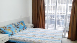 Een slaapkamer met een bed, nachtkastje, dressoir en een raam met jaloezieën.