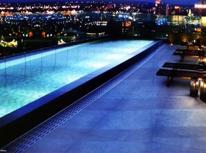 Una piscina en la azotea con vistas a un paisaje urbano nocturno.