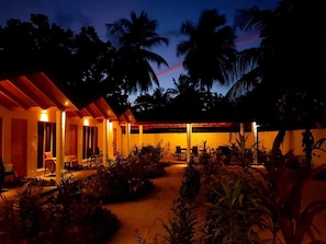 A covered outdoor area with seating and a pathway, surrounded by vegetation and palm trees. - Thoddoo Beach Holiday Inn (Thoddoo)