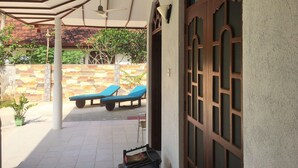 Een overdekt terras met lounge stoelen, een stenen muur en een houten deur.