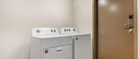 A laundry room with two white front-loading washers and a brown door.