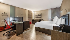 A modern hotel room with a large bed, a desk with a chair, a sofa, and a red chair.