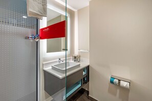 A modern bathroom with a glass shower enclosure, a large mirror, a white sink, and a towel rack.