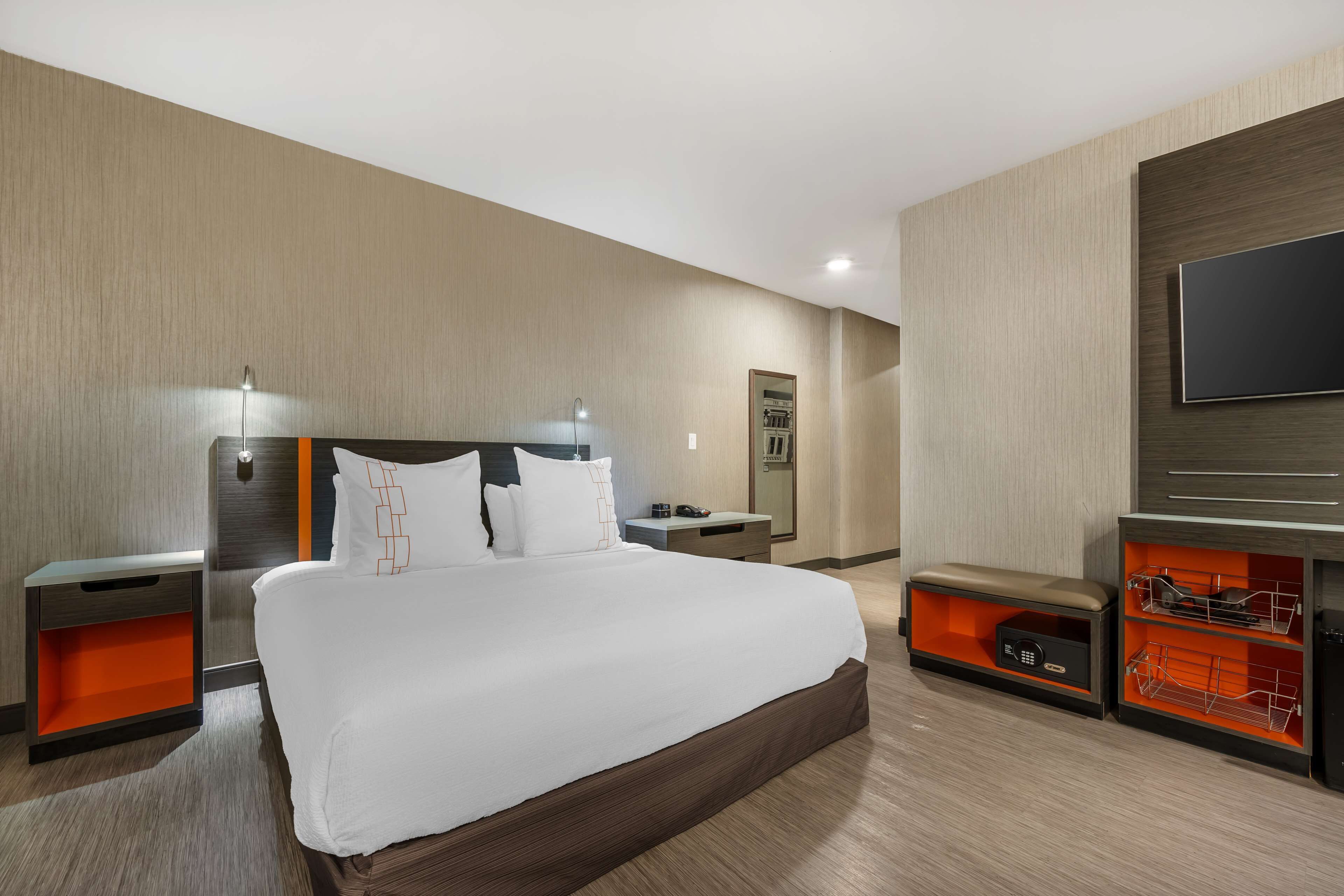 A modern hotel room with a large bed, bedside tables, a TV, and built-in storage.