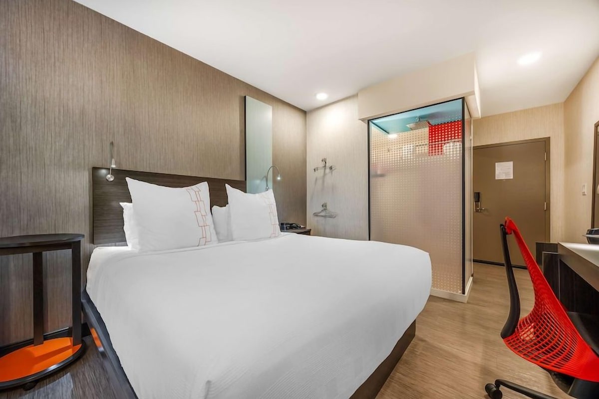 A modern hotel room with a large bed, a desk, and a shower area.
