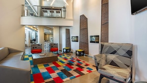 A spacious lobby with a high ceiling, a central seating area with a colorful rug, and a modern chair.