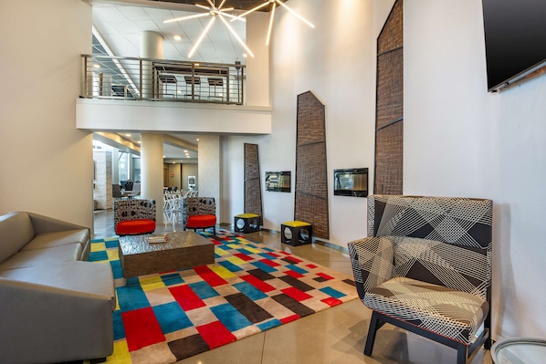 A spacious lobby with a high ceiling, a central seating area with a colorful rug, and a modern chair.