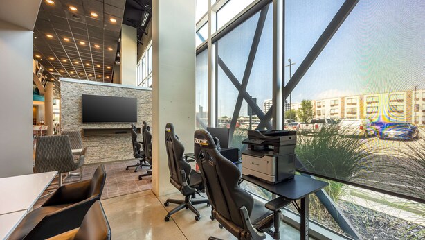 A modern office space with ergonomic chairs, a large flat-screen TV, and a view of the city through large windows.