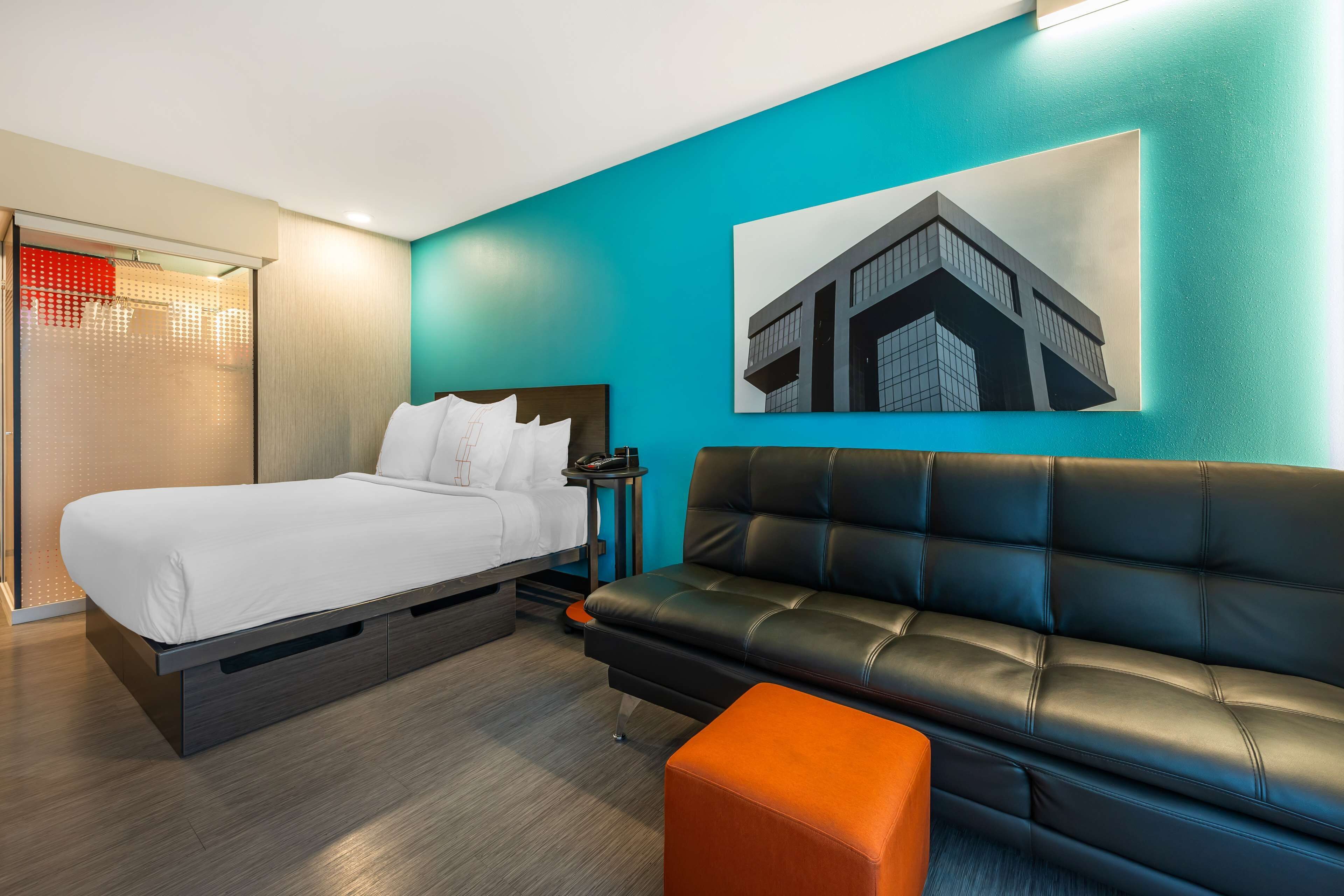 Una habitación de hotel moderna con una cama, un sofá de cuero negro y una pared de acento color aguamarina.