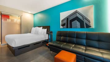 A modern hotel room with a bed, a black leather sofa, and a teal accent wall.