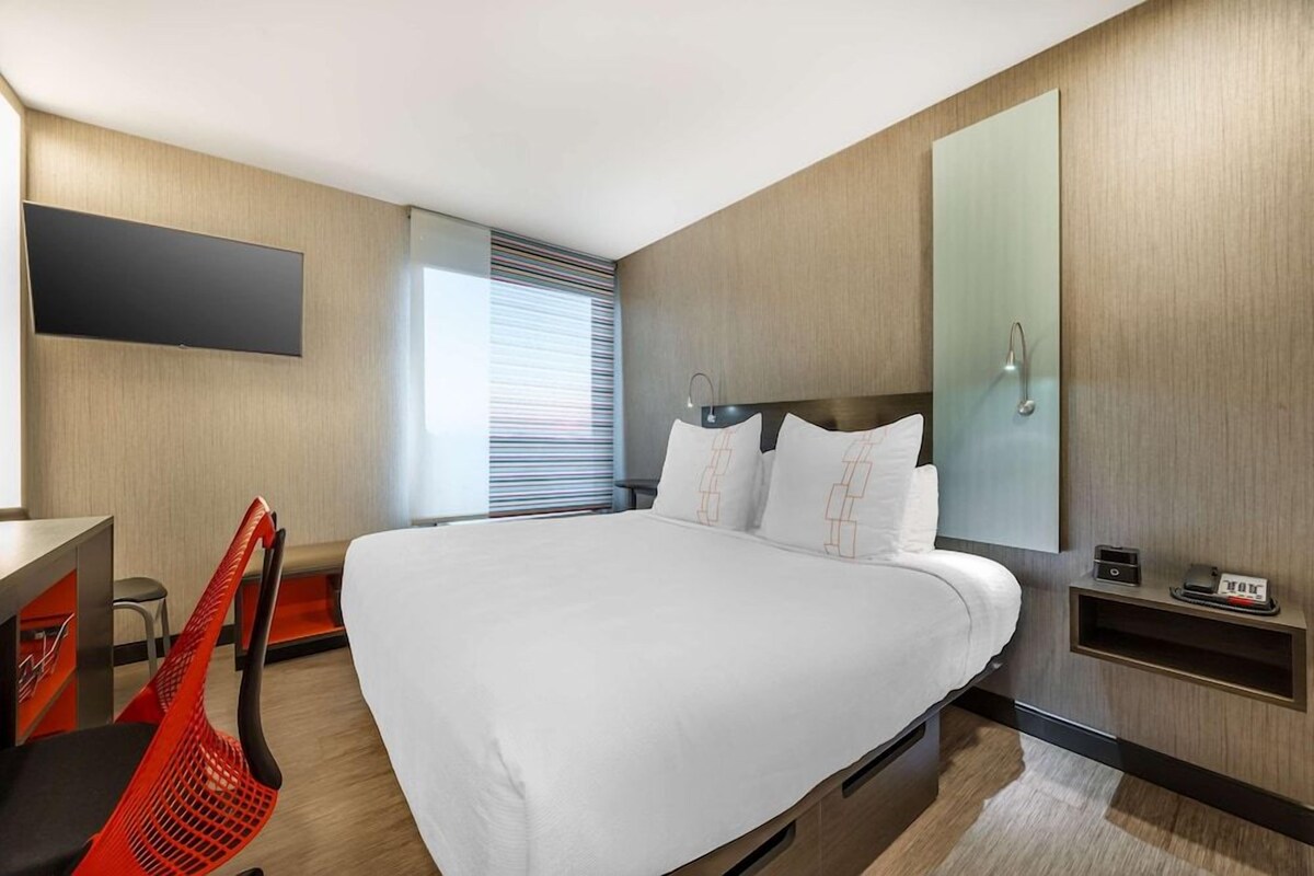 A modern hotel room with a large bed, a flat-screen TV, a shower, and a desk with a chair.