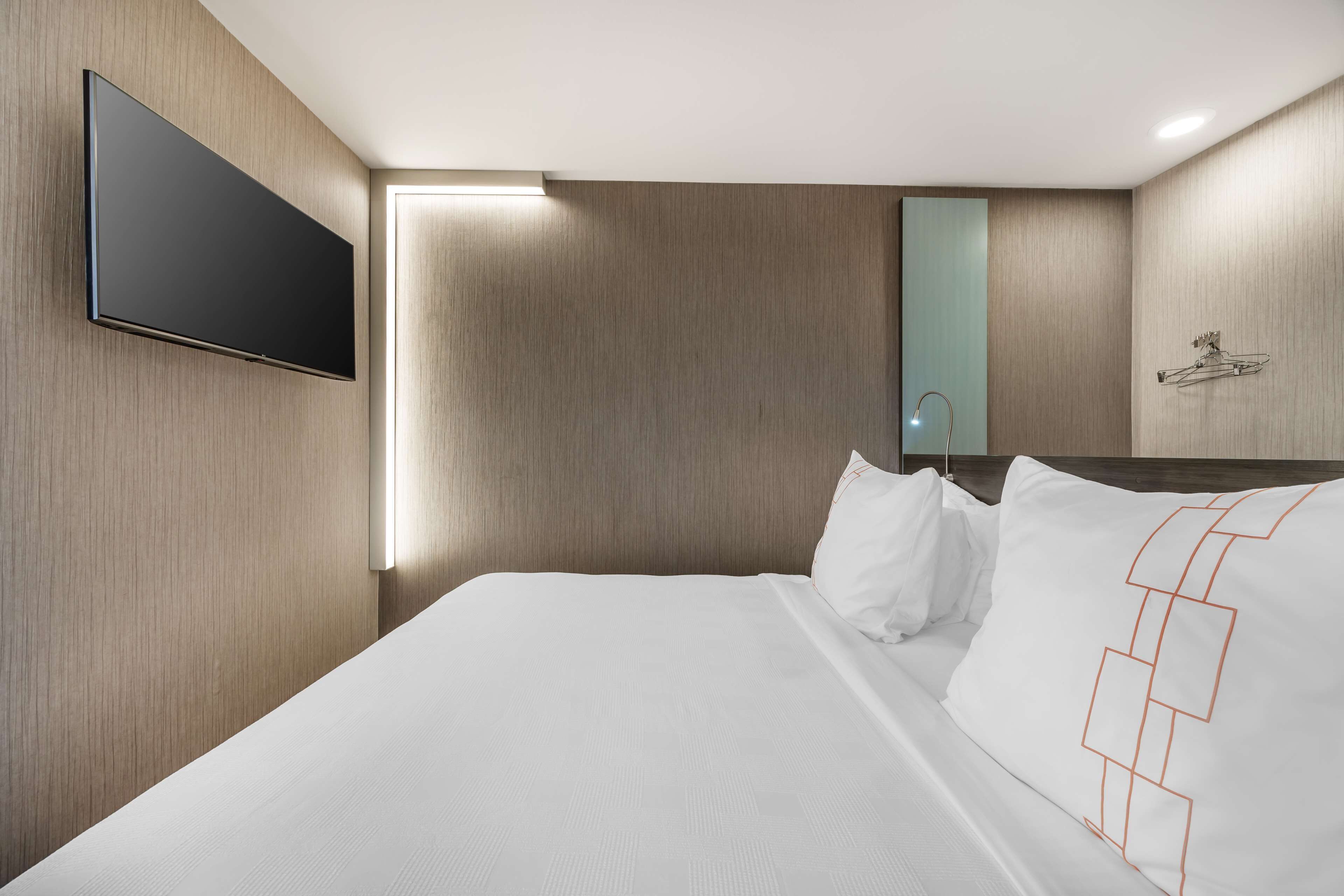 A modern hotel room with a large bed, a mounted TV, and a wooden wall panel.