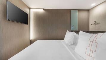 A modern hotel room with a large bed, a mounted TV, and a wooden wall panel.