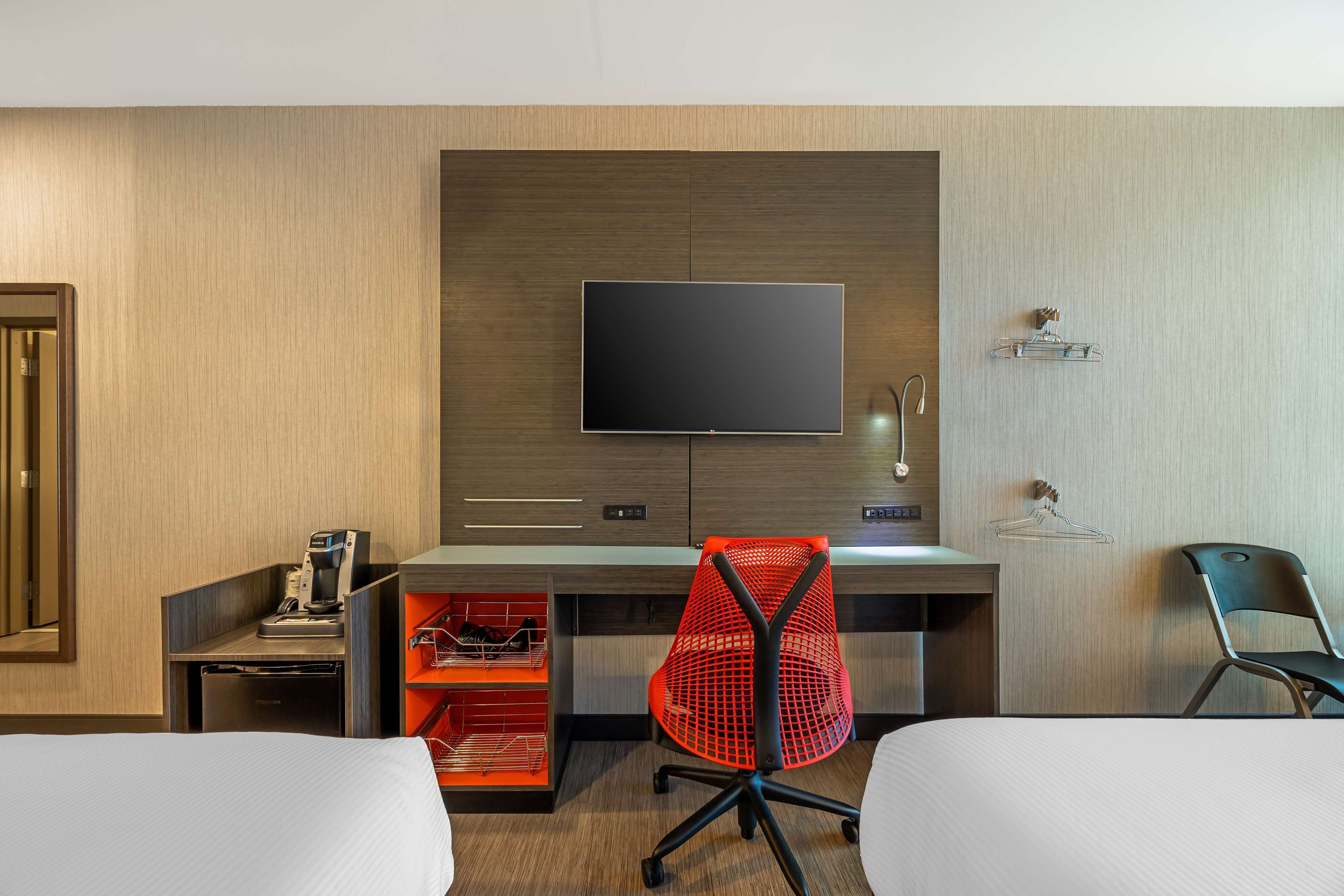 Quarto de hotel com cama, escrivaninha com computador, televisão e cadeira.