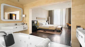 A modern hotel room with a large bathtub, a bed with a headboard, a sitting area with a chair, and a large mirror.