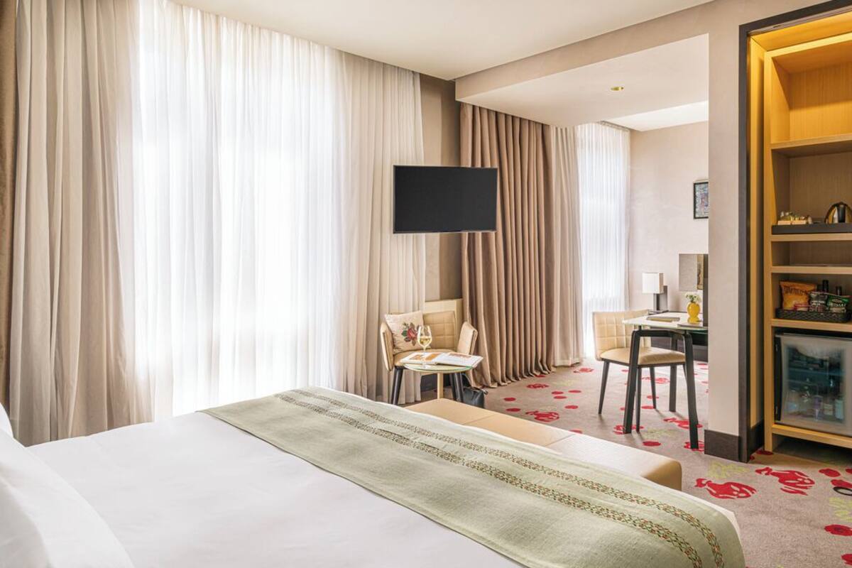 Una habitación de hotel con una cama grande, un televisor de pantalla plana, un escritorio con una silla y un minibar.