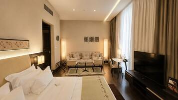 A hotel room with a bed, a sofa, a TV, and a desk with a lamp.