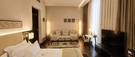 A hotel room with a bed, a sofa, a TV, and a desk with a lamp.
