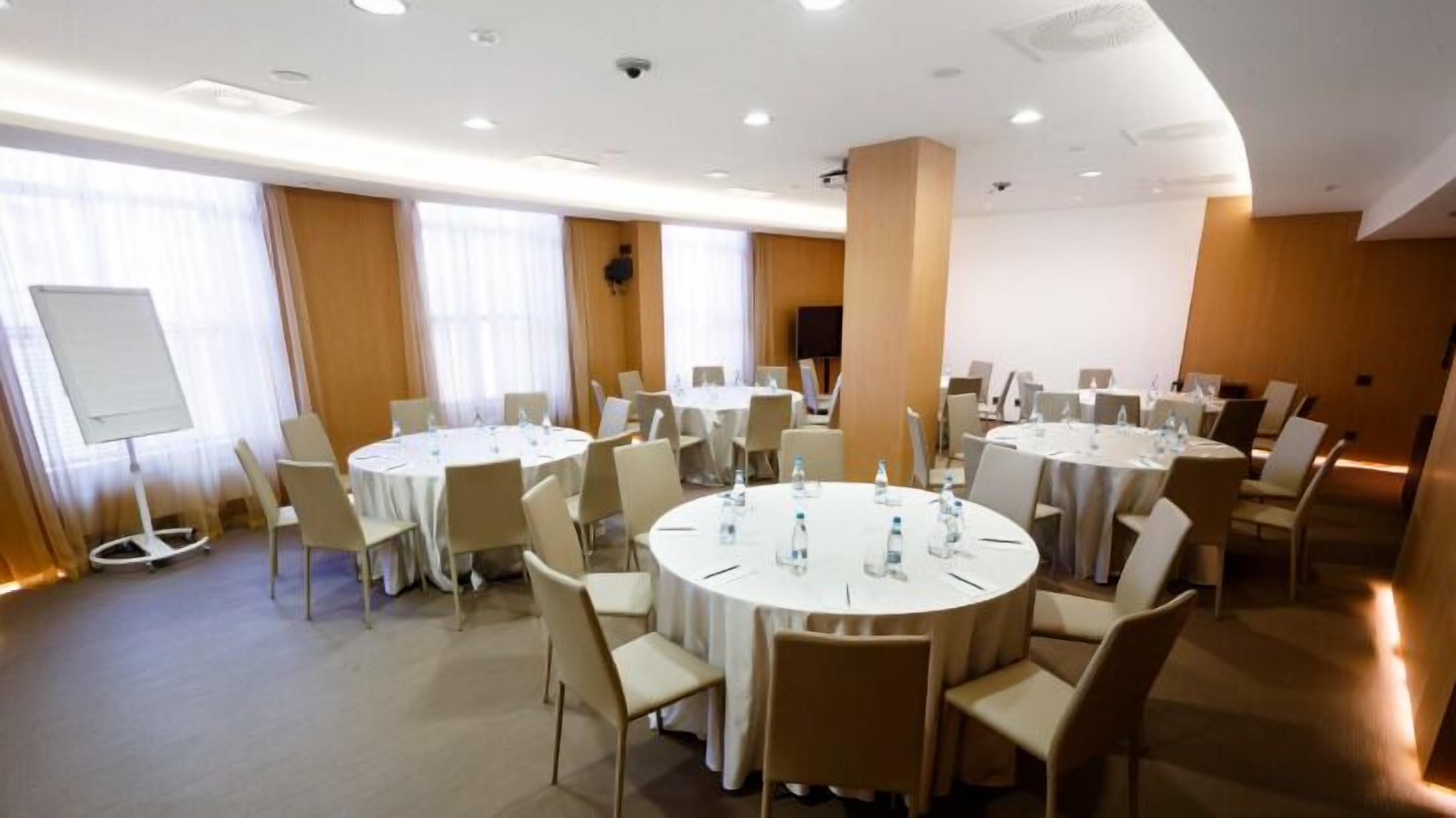 A conference room with multiple round tables, white chairs, and a whiteboard.